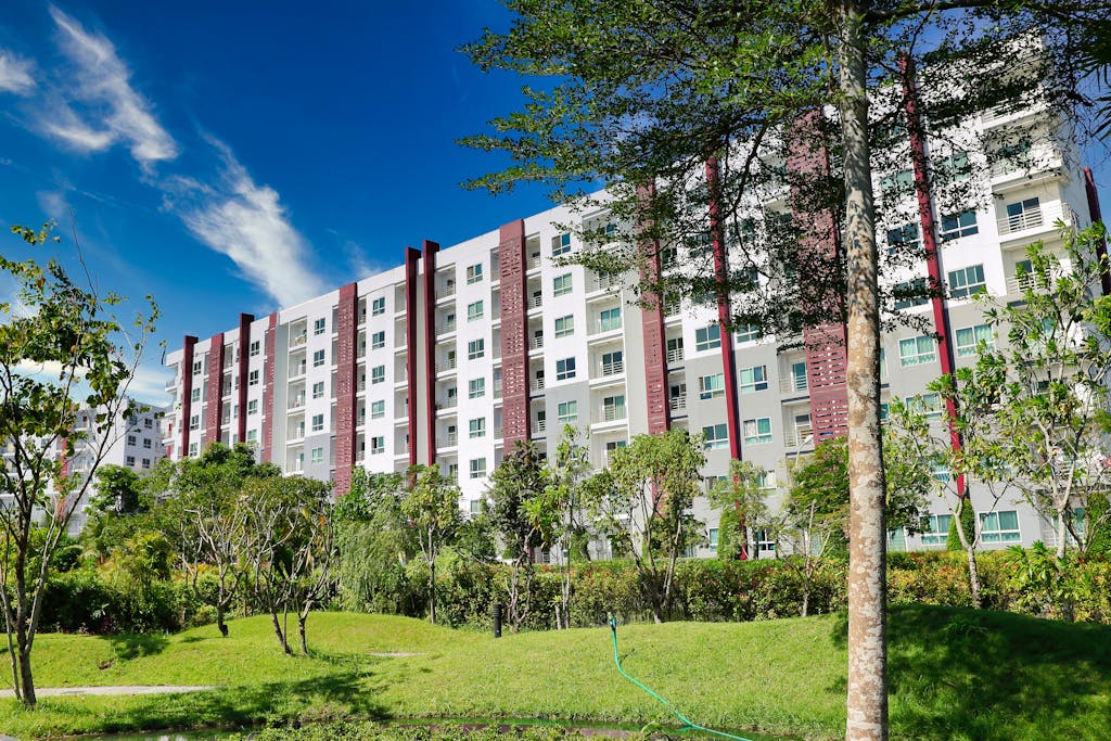 A modern apartment building surrounded by trees and greenery under a clear blue sky.