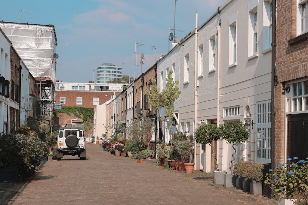 A picturesque alley featuring row houses, potted plants, and a vehicle in a city setting.
